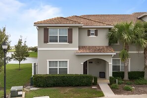 A two-story residential building with a tiled roof, a front entrance with a small archway, and a well-maintained lawn. - 5BR Storey Lake Home With Private Pool (Kissimmee)