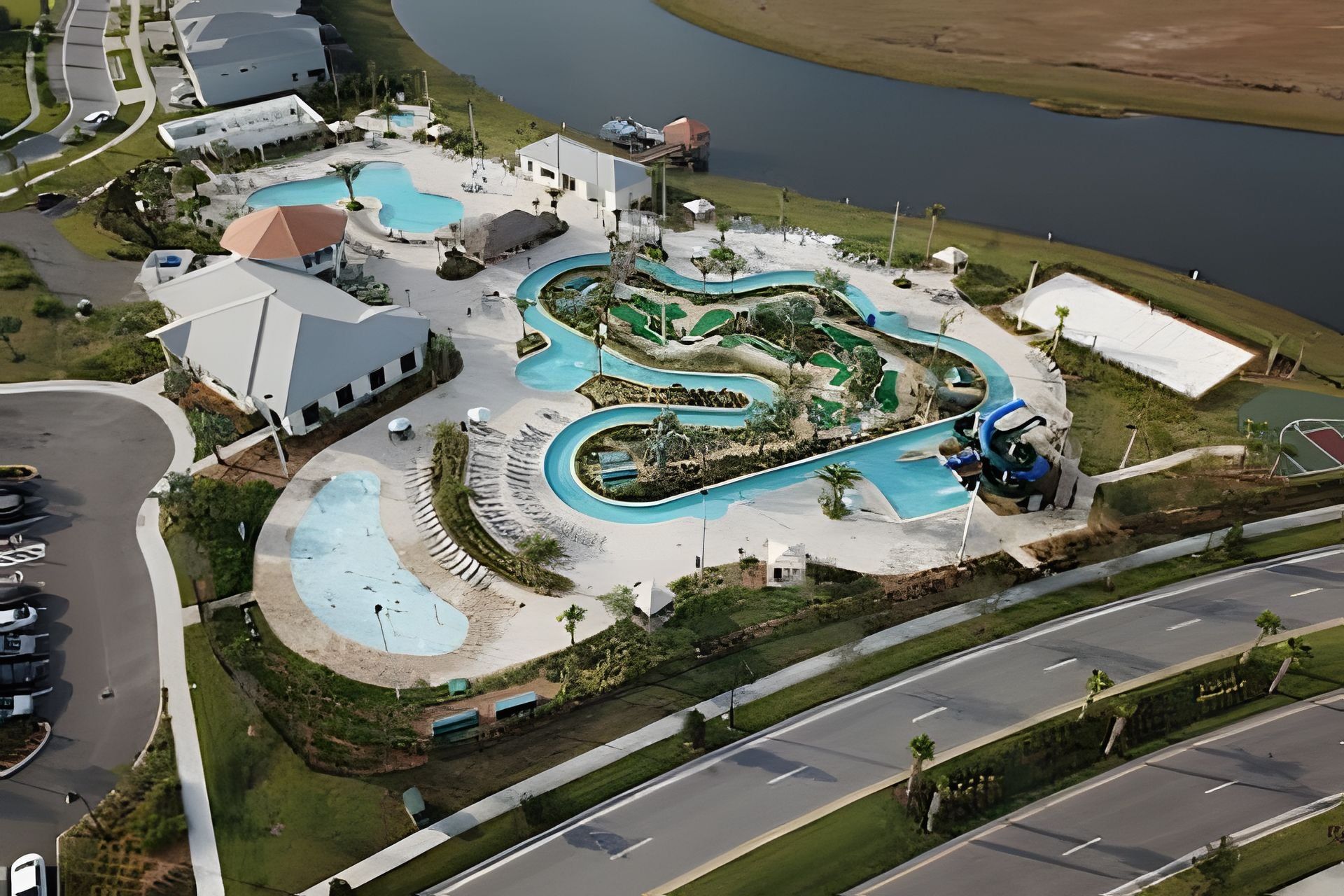 An aerial view of a resort with multiple swimming pools, a road, and a body of water.