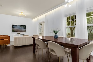 Een moderne eetruimte met een houten tafel, witte stoelen, een vaas met groen en een schilderij aan de muur.