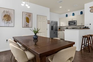 A modern kitchen with white cabinets, a stainless steel refrigerator, a microwave, and a sink. There is a dining table with chairs and a vase with a plant. - 4BR Lucaya Village Home, Sleeps 10 (Kissimmee)