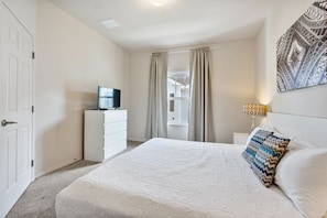 A bedroom with a large bed, a dresser, a television on the dresser, and a window with curtains. - 4BR Lucaya Village Home for Big Groups (Kissimmee)