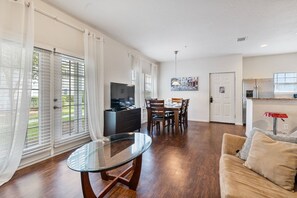 A spacious living area with a glass coffee table, a sofa, and a dining table with chairs. There is a kitchen area with a refrigerator and a sink. - 4BR Lucaya Village Home for Big Groups (Kissimmee)