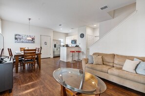 A modern living room with a glass coffee table, a beige sofa, and a dining area with wooden chairs. - 4BR Lucaya Village Home for Big Groups (Kissimmee)