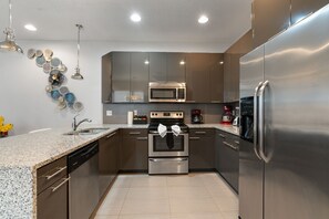 A modern kitchen with stainless steel appliances, granite countertops, and a backsplash with decorative plates. - 3BR Serenity Townhome Near Disney (Clermont)