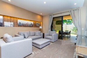 A modern living room with a grey sectional sofa, a small ottoman, and a dining area with a table and chairs. - 3BR Magic Village Townhome Near Disney (Kissimmee)