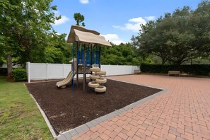 A playground with a slide and climbing structure, surrounded by a brick pathway and greenery. - 4BR Gated Home Near Disney, Sleeps 10 (Kissimmee)
