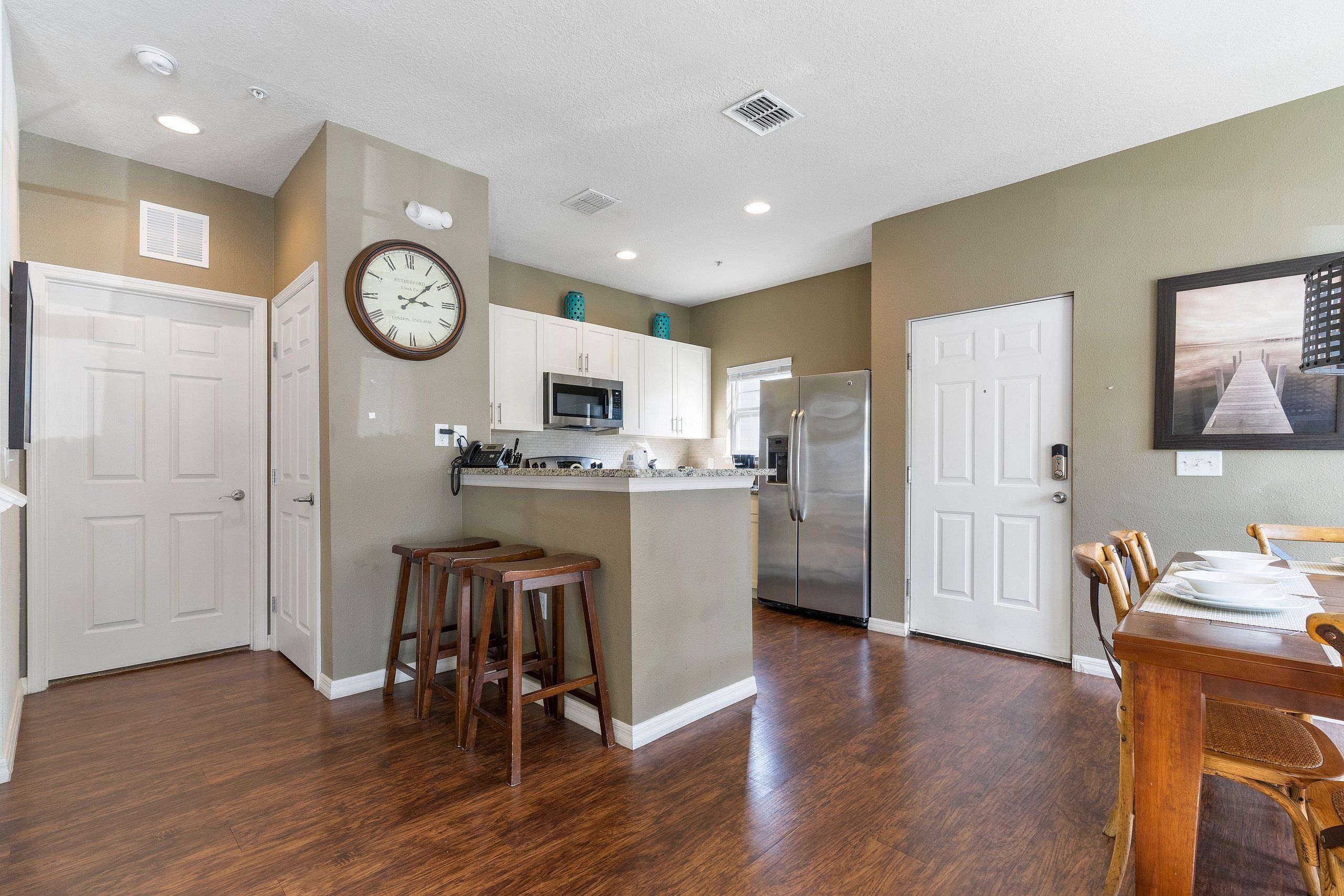 A modern kitchen with white cabinets, a stainless steel refrigerator, and a wooden dining table with bar stools.