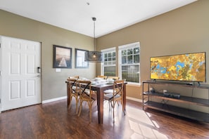 A dining area with a wooden table and chairs, a chandelier, a television on a shelf, and a door. - 4BR Lucaya Village Home, Sleeps 10 (Kissimmee)