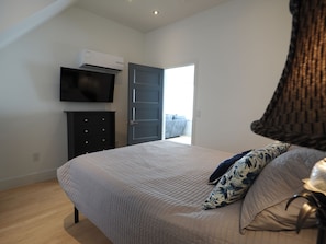 Ein Schlafzimmer mit einem Bett, einem Fernseher, einem Kleiderschrank und einer Tür, die auf einen Balkon führt.