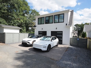 Une maison moderne à deux étages avec un garage, deux voitures blanches garées devant, et une allée bien entretenue.