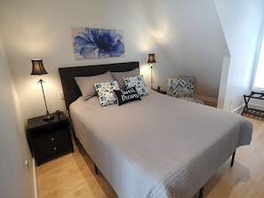 A bedroom with a bed, two nightstands, a lamp, a pillow with text, and a wall art piece. - Downtown Cary Park View Bungalow (Cary)
