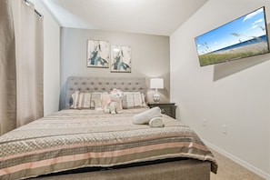 A bedroom with a large bed, a flat-screen TV mounted on the wall, and two framed artworks above the bed. - 5BR Home Near Disney With Clubhouse (Kissimmee)
