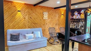 Una habitación con pared de madera con motivo de espiga, un sofá azul con cojines estampados, sillas de mimbre y una chimenea de piedra.