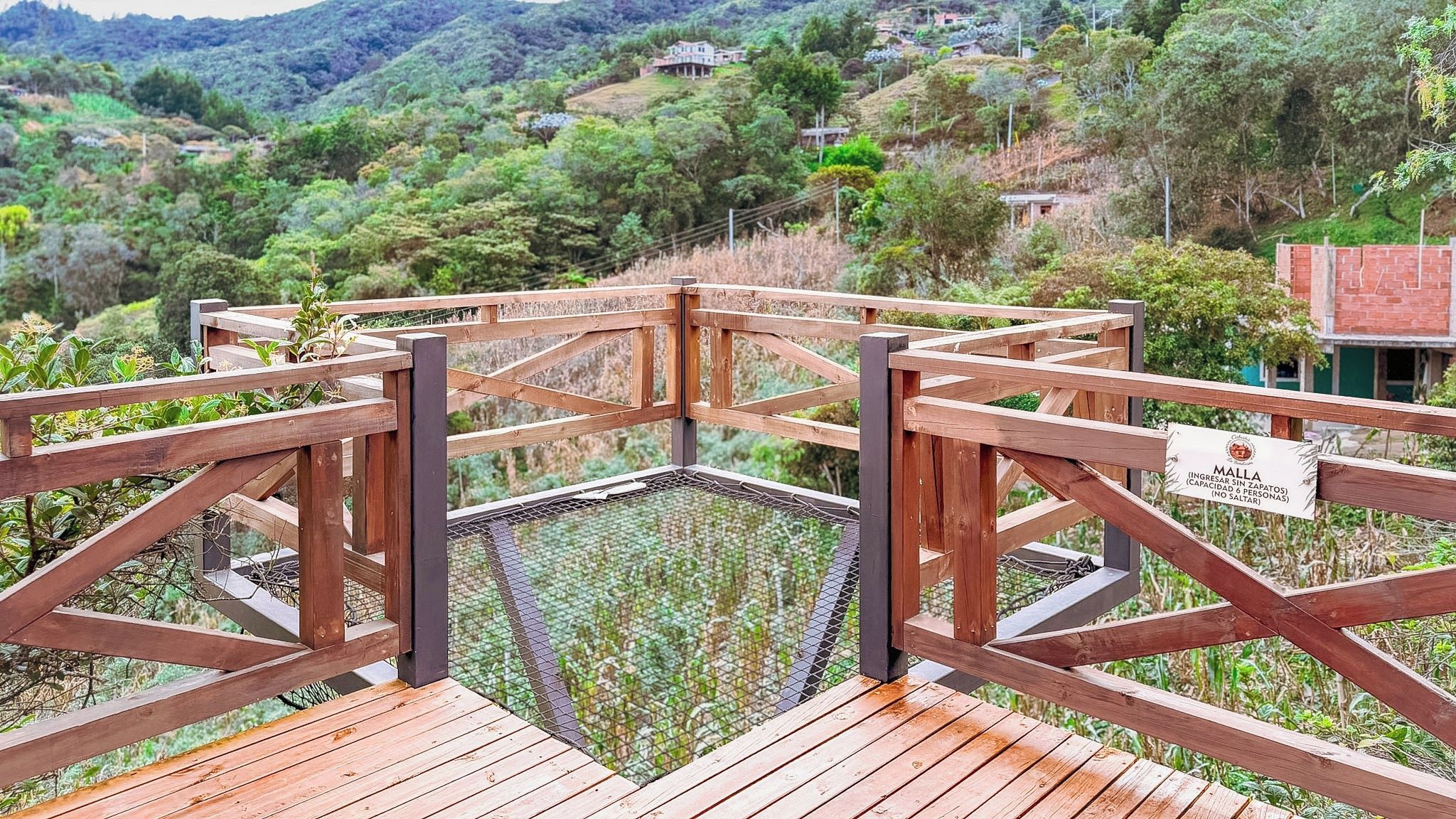 A wooden deck with a metal safety barrier, surrounded by lush greenery and hills.