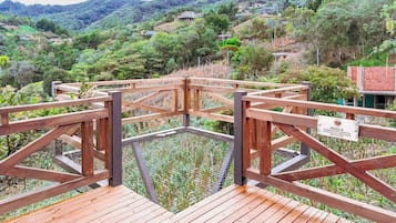 A wooden deck with a metal safety barrier, surrounded by lush greenery and hills.