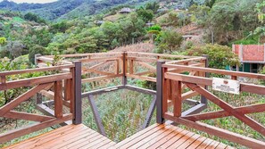 A wooden deck with a metal safety barrier, surrounded by lush greenery and hills.