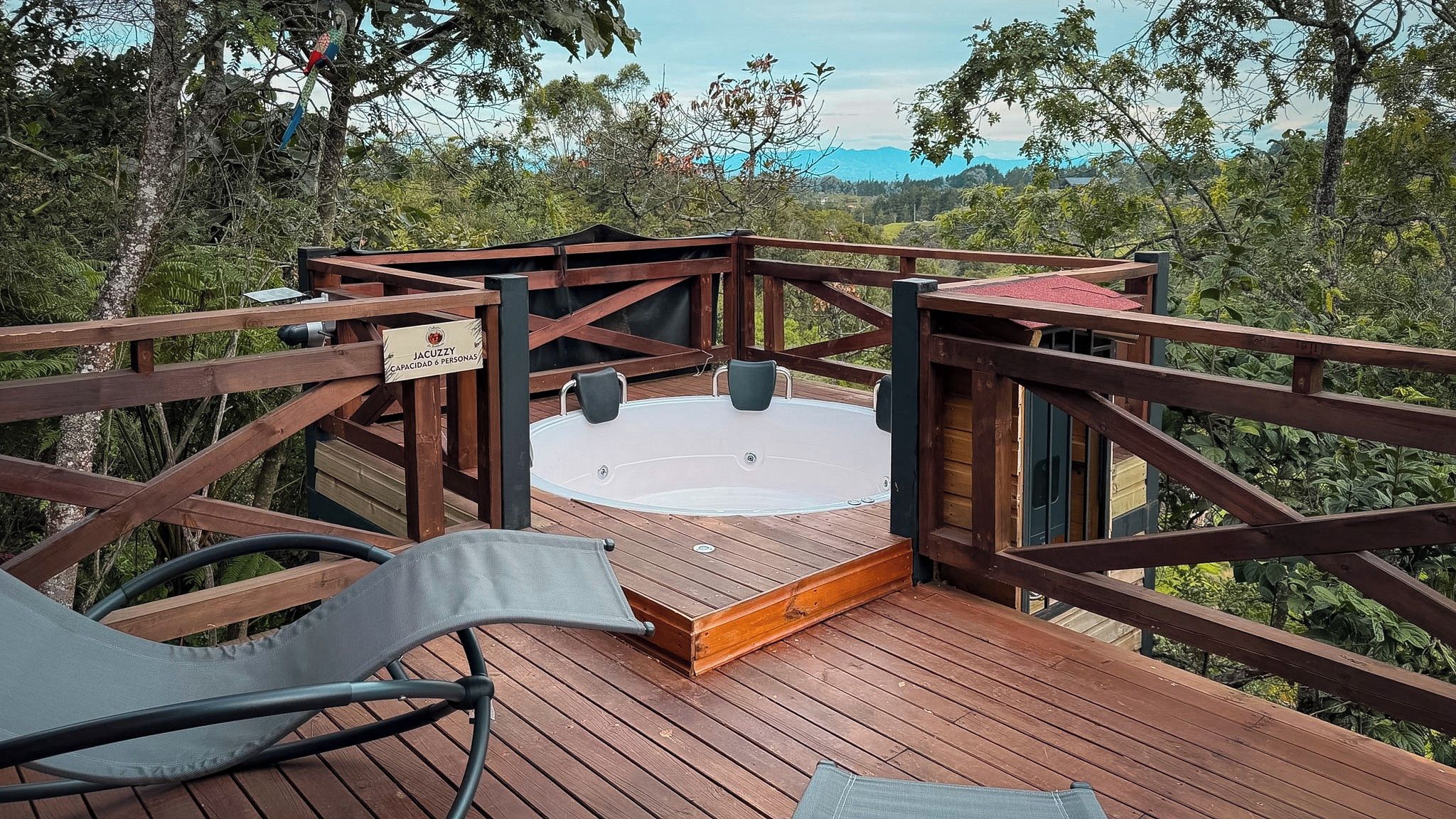 Een houten terras met een hottub, omgeven door een houten balustrade, met uitzicht op een bebost gebied.