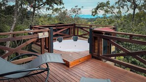 Una terraza de madera con un jacuzzi, rodeada por barandas de madera, con vistas a un área boscosa.