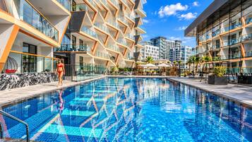 A swimming pool with clear blue water, surrounded by modern buildings with balconies and outdoor seating areas.
