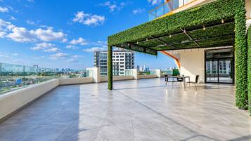A rooftop terrace with a view of the city skyline, a glass railing, and a seating area.