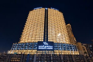 Um edifício alto com fachada geométrica marcante, iluminado à noite.