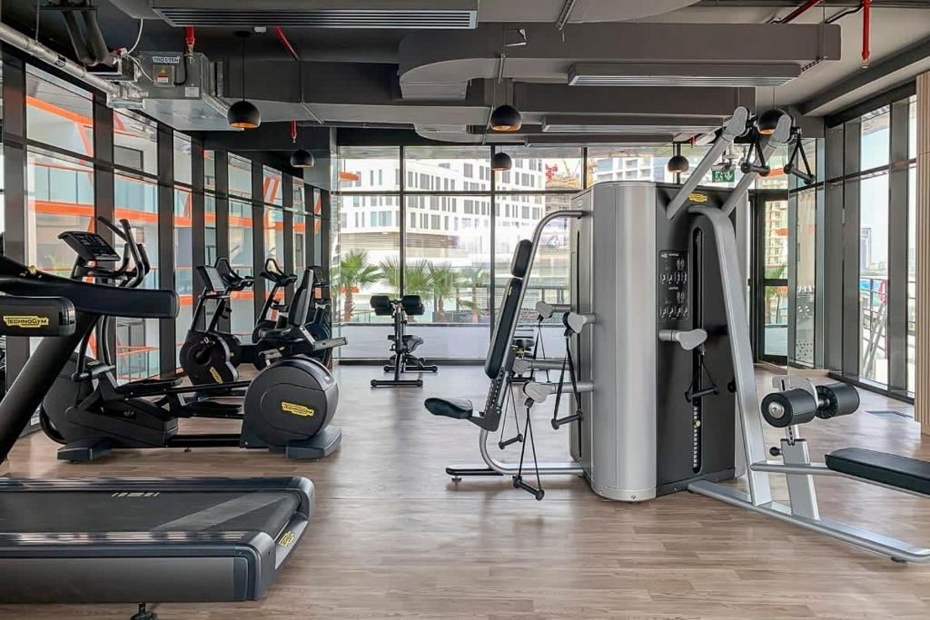 Een fitnessruimte met cardioapparaten, gewichten en grote ramen met uitzicht op de stad.