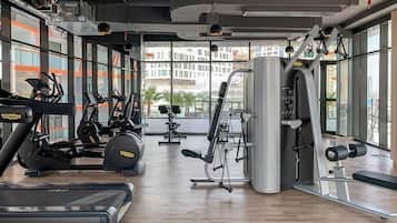 Een fitnessruimte met cardioapparaten, gewichten en grote ramen met uitzicht op de stad.
