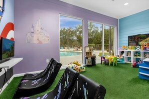 A room with a large window, a pool view, and a children's play area with toys and a small table. - 4BR Lucaya Home w/ Disney Themes + Clubhouse (Kissimmee)