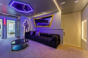 A modern living room with a dark-colored sofa, a glass coffee table, and a Star Wars-themed wall decoration. - 5BR Villa w/ Pool, Themed Rooms Windsor Island (Davenport)