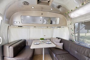 A compact RV interior with a dining area, seating, and a window. - The Tidal Tin - Private Marshside Airstream Retreat Near Beaufort (Beaufort)