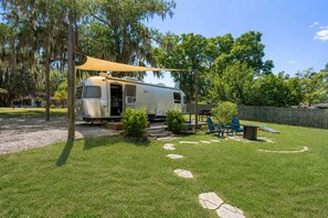 A recreational vehicle (RV) parked in a backyard with a patio area, outdoor seating, and a barbecue grill. - The Tidal Tin - Private Marshside Airstream Retreat Near Beaufort (Beaufort)