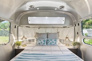 Un intérieur de camping-car compact comprenant un lit, deux tables de chevet, deux lampes et une fenêtre.
