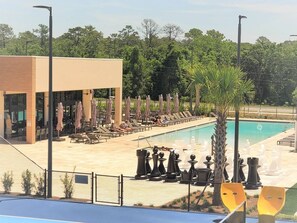 A pool area with lounge chairs and umbrellas, a building with large windows, and a fenced pool. - Elegant 4BR Home Near Disney Magic Village Views (Kissimmee)