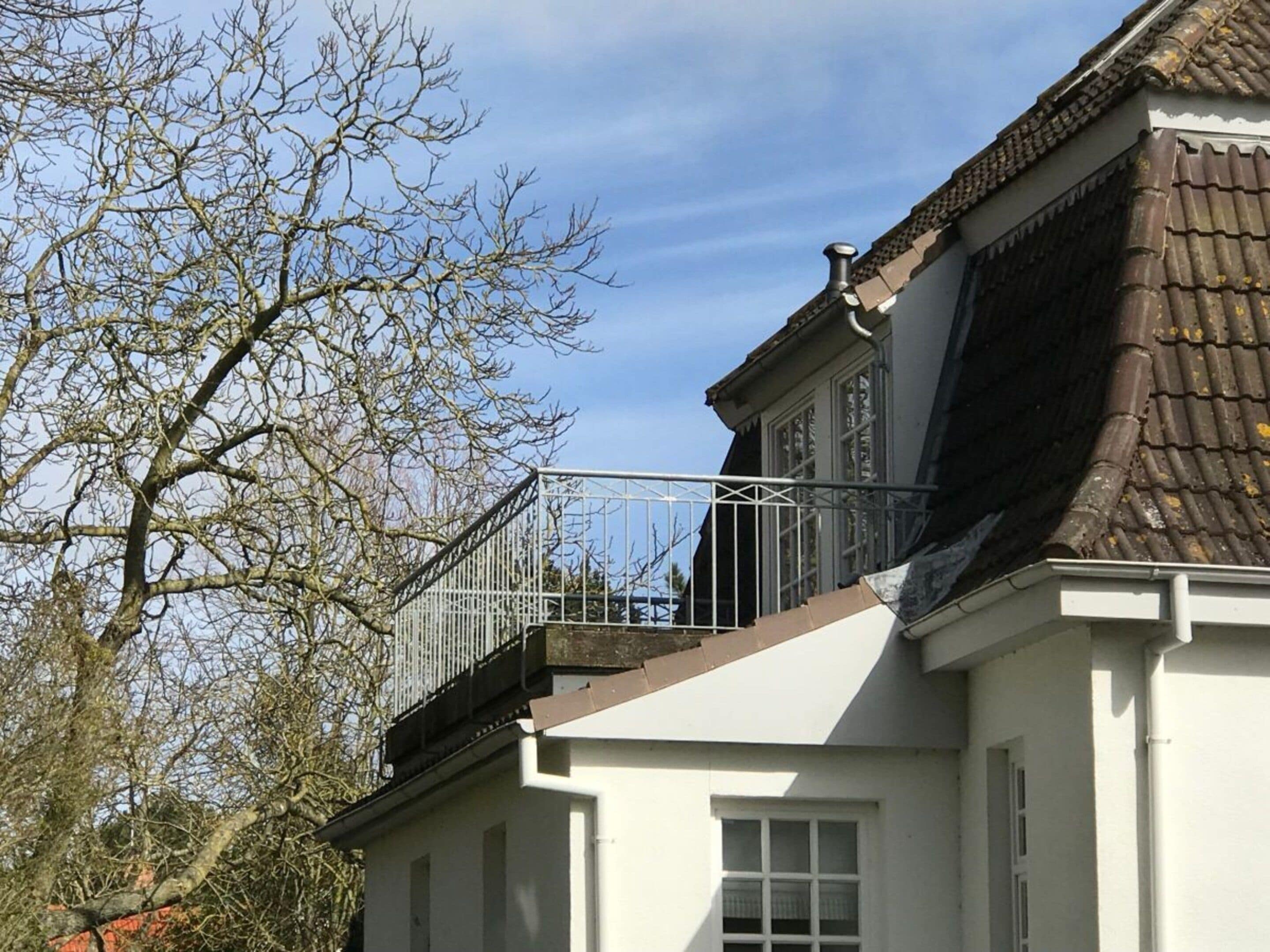 Een gebouw met een witte gevel, een bruin dak en een metalen balkonhek.