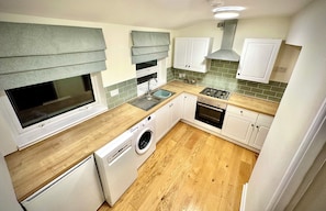 A compact kitchen with a washing machine, a sink, and a stove. - Cosy Cottage on the Cotswold way with Amazing views.  (Dursley)
