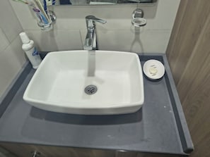A bathroom sink with a chrome faucet, a soap dish, and a bottle of oral care product on the countertop. - Vrbo Property (Batumi)