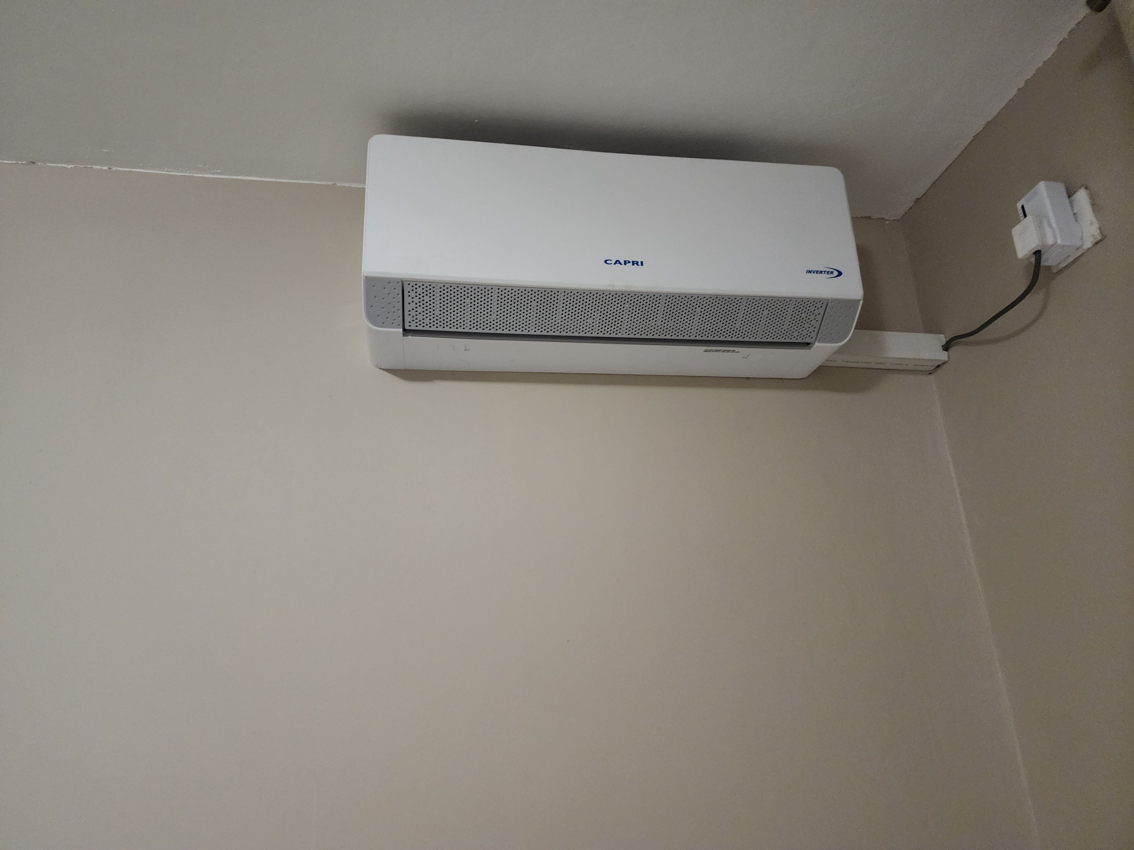 A white air conditioning unit mounted on a wall with a power cord plugged in.