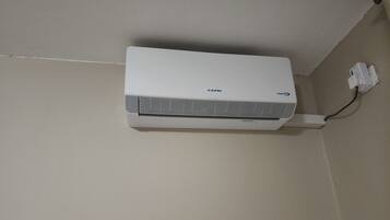A white air conditioning unit mounted on a wall with a power cord plugged in.