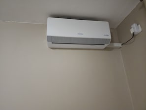 A white air conditioning unit mounted on a wall with a power cord plugged in.