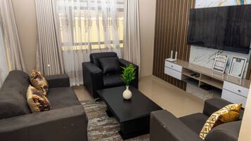 A modern living room with a black sofa set, a coffee table with a plant, a flat-screen TV, and a wooden accent wall.