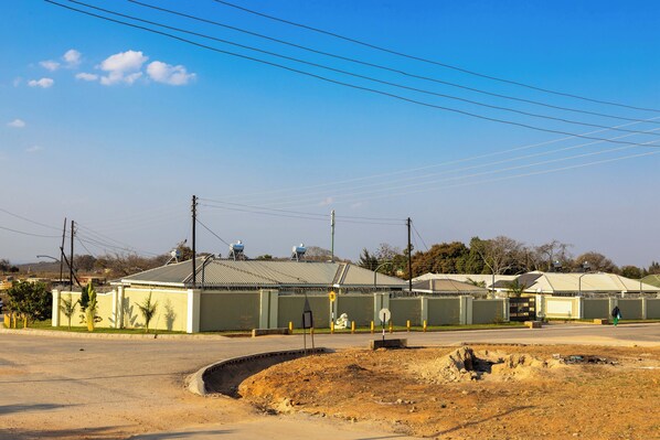 A building with a flat roof, surrounded by a fence, and a road in the foreground.