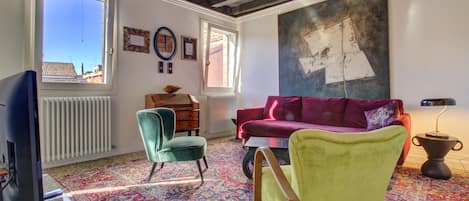 A living room with a sofa, chairs, a television, and a large painting on the wall.