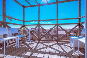 Eine private Dachterrasse mit Holzboden, weißen Stühlen und Blick auf die Stadtlandschaft.