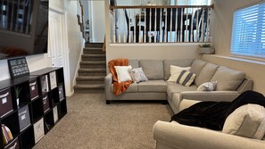 Ein Wohnzimmer mit einer Eckcouch, einem Bücherregal und einer Treppe, die eine weitere Ebene hinaufführt.