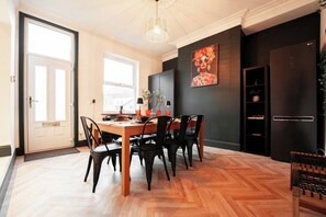 A dining area with a wooden table and chairs, a black-framed picture on the wall, and a black refrigerator. - The Gathering House - Beautiful Large House Suits Contractors (Leeds)