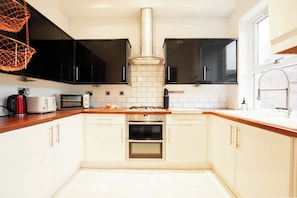 A modern kitchen with black cabinets, a white tiled backsplash, stainless steel appliances, and a wooden countertop. - The Gathering House - Beautiful Large House Suits Contractors (Leeds)
