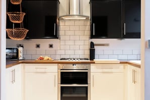 A kitchen with black cabinets, white tiles, a stove, oven, and a microwave. - The Gathering House - Beautiful Large House Suits Contractors (Leeds)