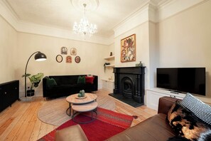 A living room with a black sofa, a round coffee table, a fireplace, and a television. - The Gathering House - Beautiful Large House Suits Contractors (Leeds)