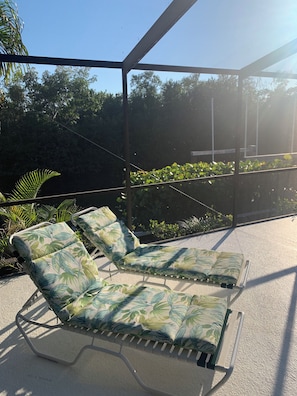 A covered outdoor seating area with lounge chairs and a view of greenery. - 3-bedroom house on canal, gated community, private beach access on Longboat Key! (Longboat Key)
