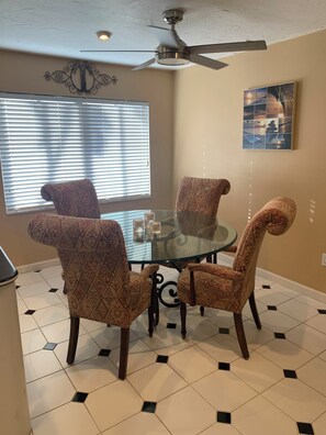 A dining area with a glass table surrounded by patterned chairs, a ceiling fan, and a wall-mounted artwork. - 3-bedroom house on canal, gated community, private beach access on Longboat Key! (Longboat Key)